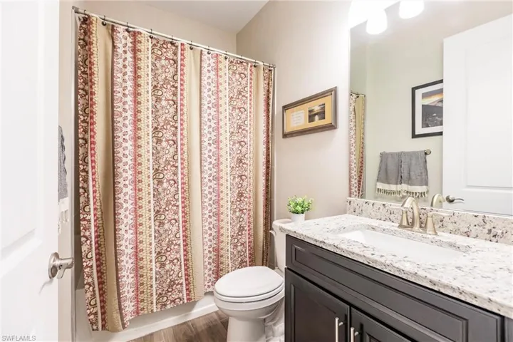Guest bathroom with plank tile flooring, toilet, and large vanity