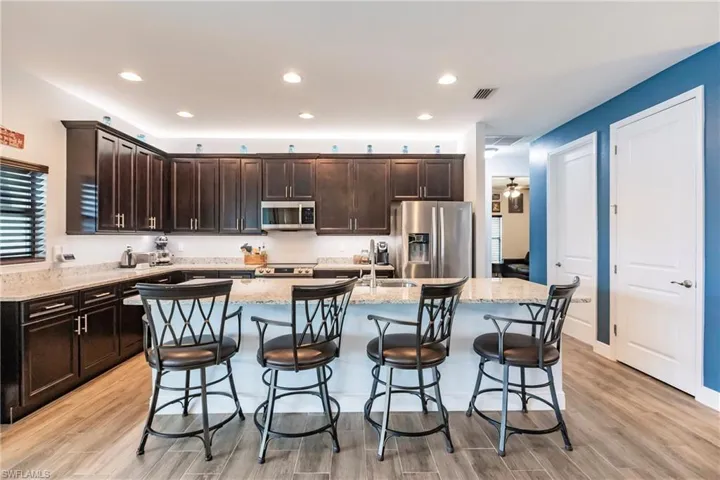 Kitchen featuring an island with sink, stainless steel appliances, plank tile flooring, and light stone countertops