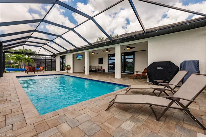 View of swimming pool with ceiling fan, glass enclosure, and a patio