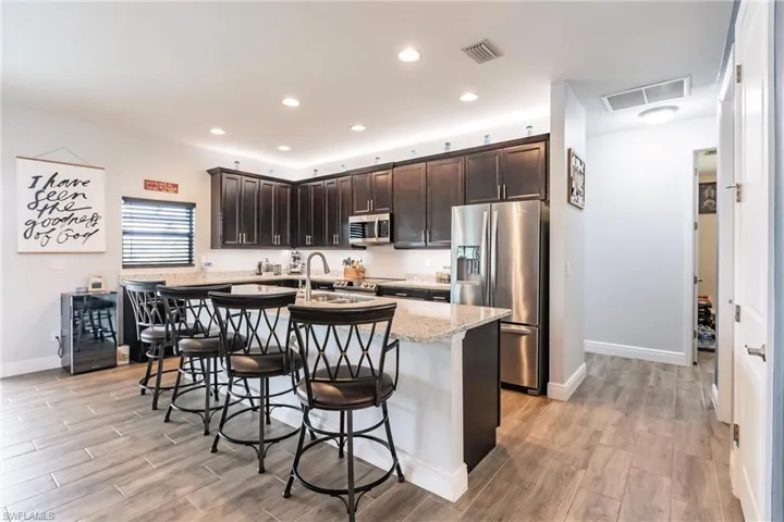 Kitchen with plank tile floors, a kitchen breakfast bar, a center island with sink, and stainless steel appliances