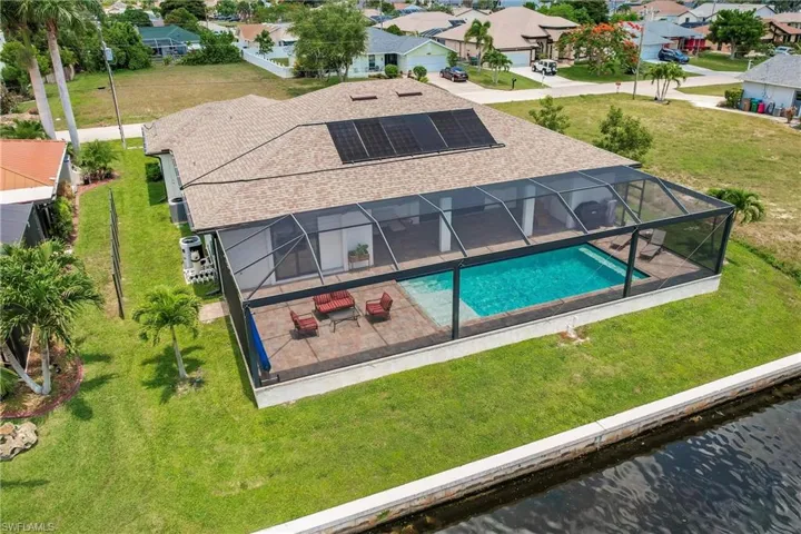 Rear view of house with a water view, a patio area, solar panels, a yard, and glass enclosure