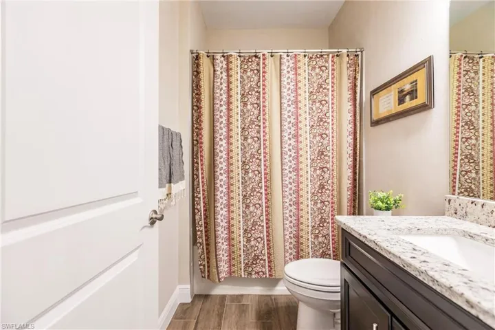 Guest bathroom with plank tile flooring, toilet, and large vanity