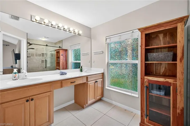 Full bath featuring a shower stall, double vanity, and light tile patterned floors