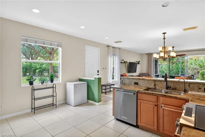 Kitchen featuring brown cabinetry, dark stone counters, appliances with stainless steel finishes, decorative light fixtures, and a chandelier