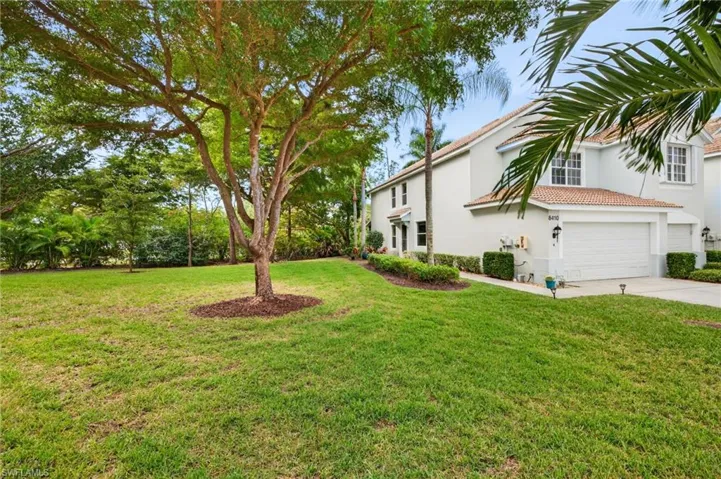 View of green lawn with concrete driveway and a garage