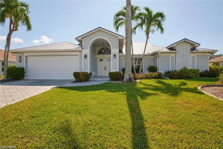 Ranch-style home with metal roof, a garage, a front yard, and decorative driveway