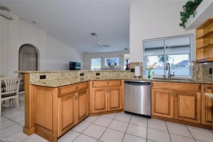 Kitchen with vaulted ceiling, light stone counters, dishwasher, a sink, and brown cabinets