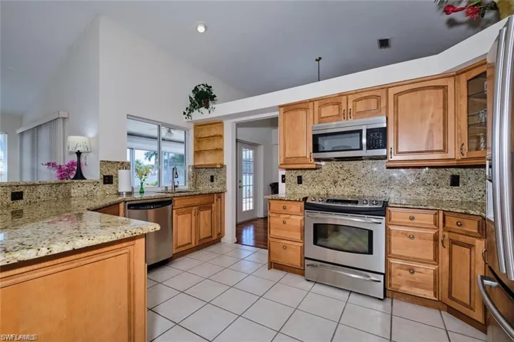 Kitchen featuring light tile patterned floors, light stone countertops, vaulted ceiling, appliances with stainless steel finishes, and backsplash