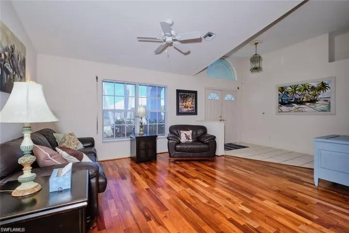 Living area with lofted ceiling, visible vents, ceiling fan, and wood finished floors