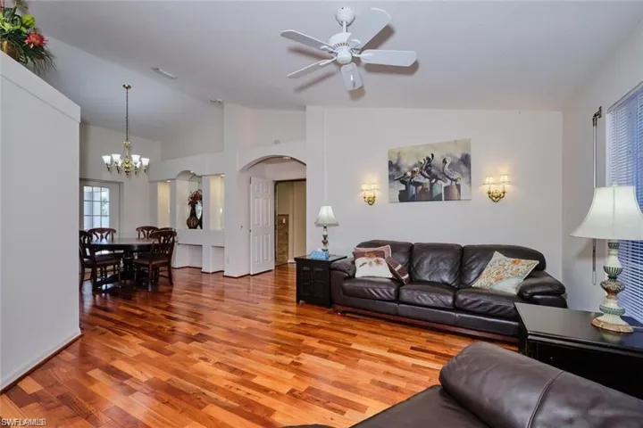 Living area with visible vents, arched walkways, ceiling fan with notable chandelier, vaulted ceiling, and wood finished floors