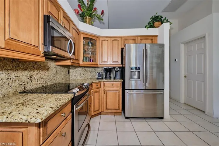 Kitchen featuring tasteful backsplash, light stone counters, light tile patterned floors, glass insert cabinets, and appliances with stainless steel finishes