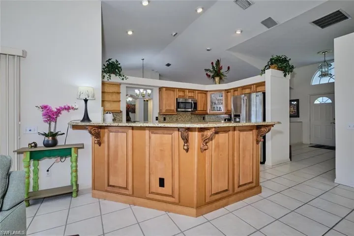 Kitchen featuring vaulted ceiling, light stone counters, visible vents, a breakfast bar area, and stainless steel appliances