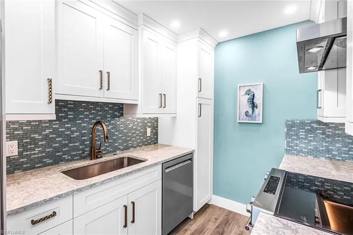 Kitchen featuring stainless steel appliances, a sink, light wood-type flooring, white cabinets, and decorative backsplash