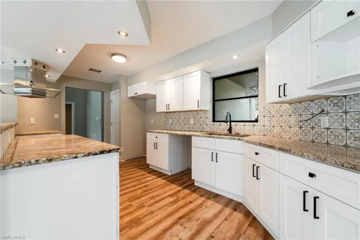 Kitchen with stone counters, light hardwood / wood-style floors, white cabinets, and sink