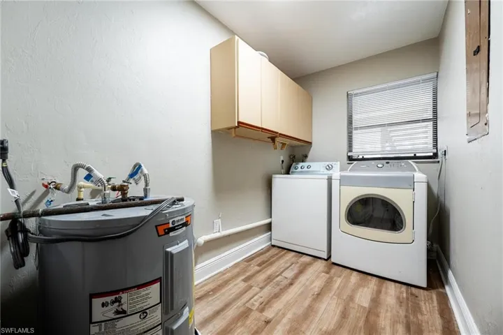 Laundry room featuring washing machine and dryer, cabinets, water heater, and light wood-type flooring