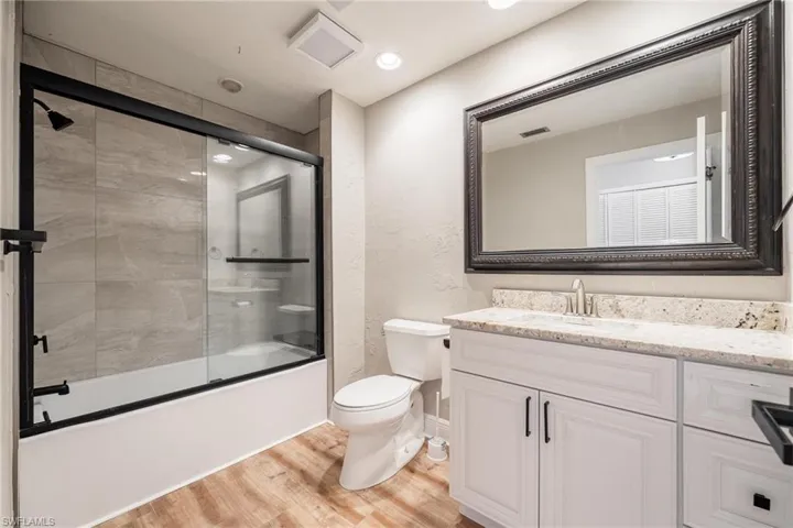 Full bathroom featuring hardwood / wood-style flooring, vanity, toilet, and enclosed tub / shower combo