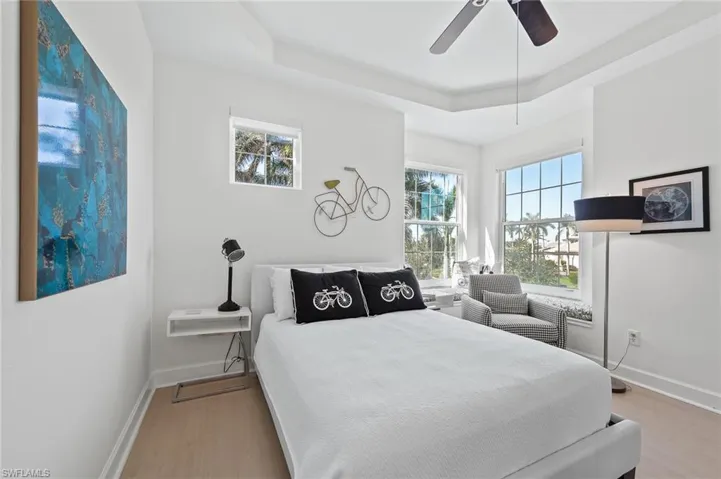 Bedroom with multiple windows, light wood-style flooring, a ceiling fan, and a tray ceiling