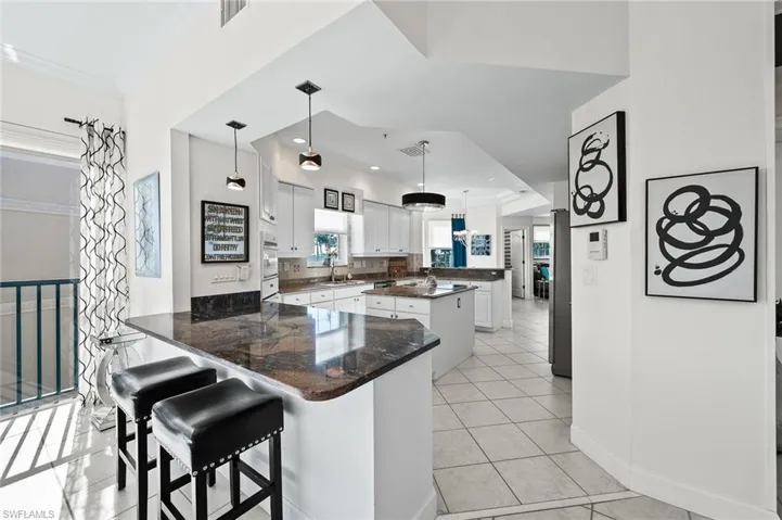 Kitchen with a peninsula, a kitchen island, a kitchen bar, white cabinets, and decorative light fixtures