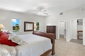 Bedroom featuring a ceiling fan, light tile patterned floors, multiple windows, and attic access