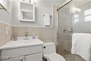 Full bathroom featuring vanity, a shower stall, tile walls, wainscoting, and a chandelier