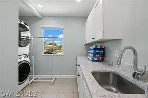 Laundry room with stacked washer / dryer, cabinet space, light tile patterned flooring, and recessed lighting