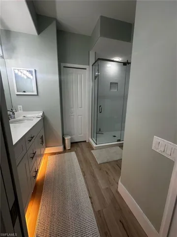 Full bathroom featuring a stall shower, double vanity, and wood finished floors