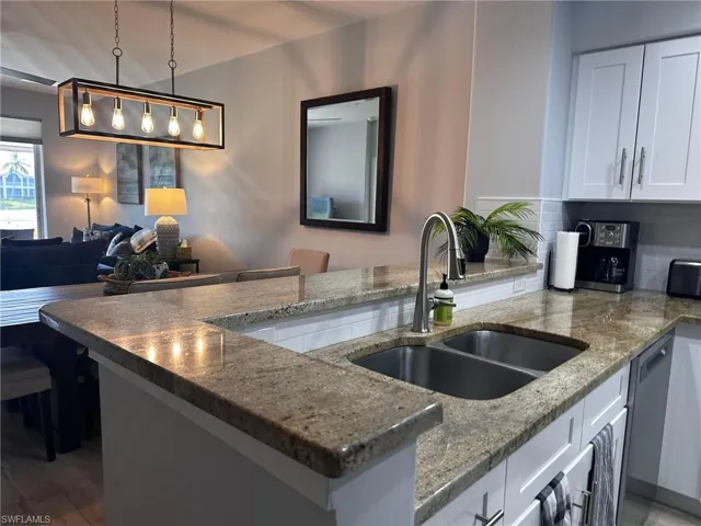 Kitchen featuring backsplash, white cabinets, stainless steel dishwasher, decorative light fixtures, and dark stone counters