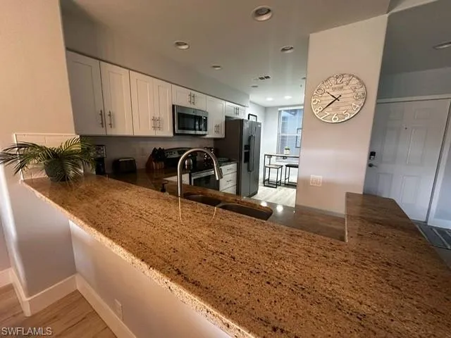 Kitchen with stone counters, light wood finished floors, appliances with stainless steel finishes, a peninsula, and recessed lighting