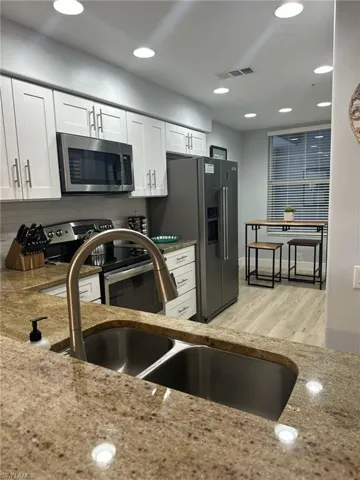 Kitchen with appliances with stainless steel finishes, white cabinets, recessed lighting, light wood finished floors, and light stone counters