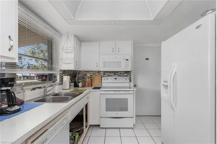 Kitchen featuring white appliances, white cabinets, sink, tasteful backsplash, and light tile floors