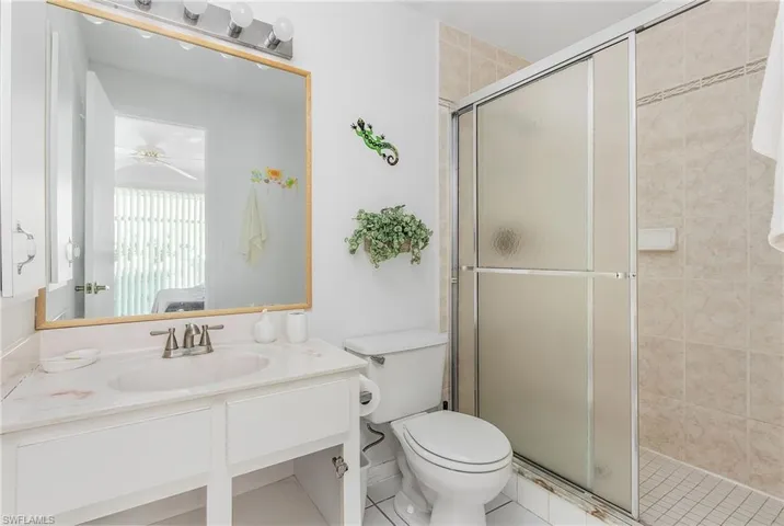 Bathroom featuring a shower with door, ceiling fan, toilet, and vanity