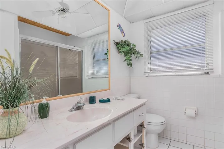 Bathroom featuring tile floors, toilet, tile walls, ceiling fan, and oversized vanity