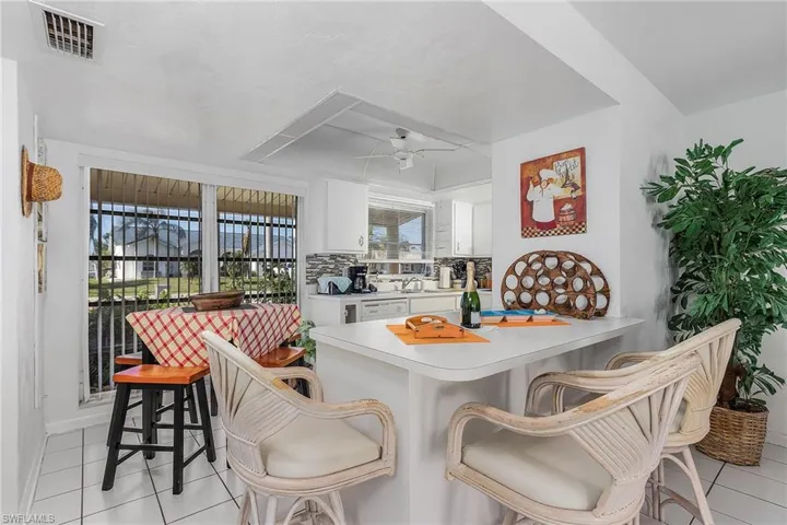 Kitchen featuring a kitchen breakfast bar, backsplash, white cabinetry, and light tile floors