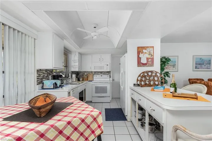 Kitchen featuring ceiling fan, tasteful backsplash, white appliances, light tile flooring, and white cabinetry