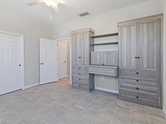 Unfurnished bedroom featuring built in desk, ceiling fan, and light tile floors