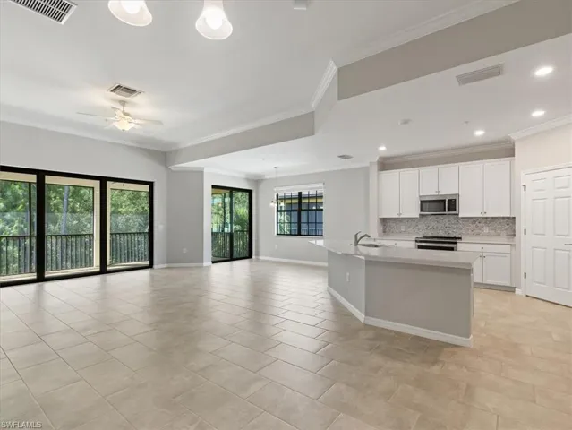 Kitchen featuring backsplash, stove, white cabinetry, an island with sink, and ornamental molding