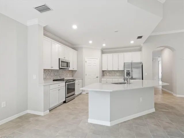 Kitchen featuring appliances with stainless steel finishes, white cabinets, backsplash, and an island with sink