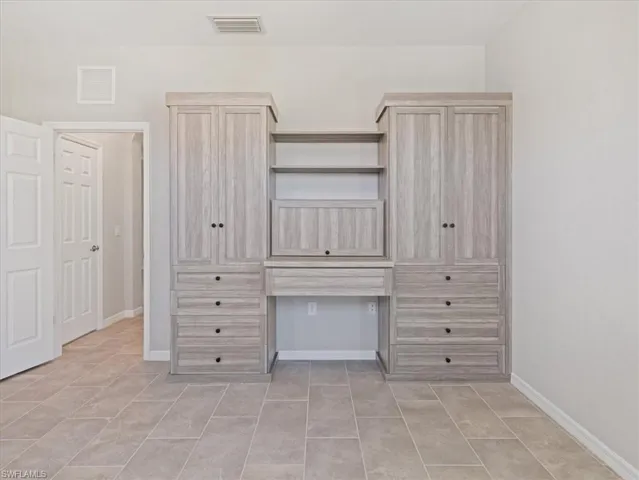 Unfurnished bedroom with built in desk and light tile floors
