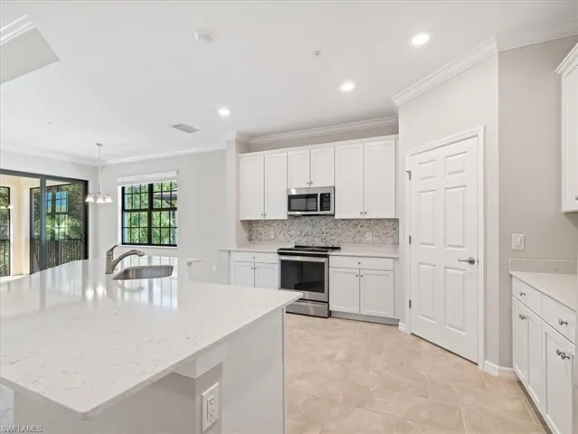 Kitchen with quartz island with sink, stainless steel appliances, light tile floors, hanging light fixtures, and sink