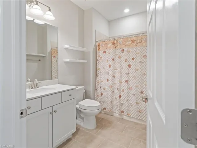 Bathroom with tile flooring, oversized vanity, and toilet and shelving