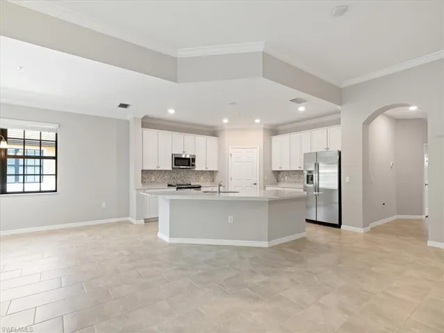 Kitchen with appliances with stainless steel finishes, white cabinets, light tile floors, and an island with sink