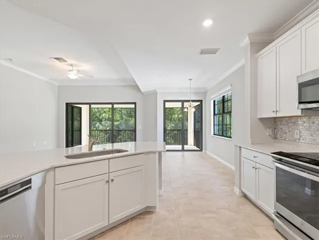 Kitchen with sink, a healthy amount of sunlight, light tile floors, and appliances with stainless steel finishesSliding doors to lanai with preserve view.  High impact glass!