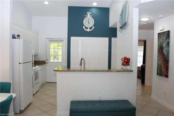 Kitchen featuring kitchen peninsula, light tile patterned floors, white cabinets, and white appliances