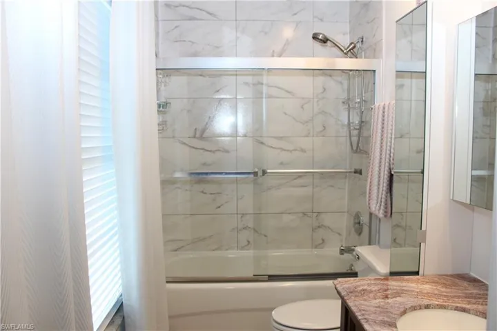 Full bathroom with shower / bath combination with glass door, vanity, and toilet