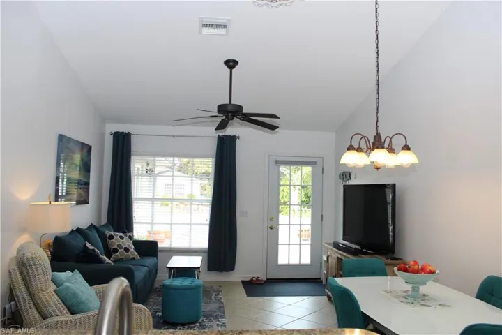 Tiled living room featuring ceiling fan with notable chandelier, a wealth of natural light, and lofted ceiling