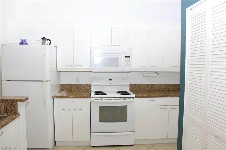 Kitchen with dark stone countertops, white cabinets, light tile patterned flooring, and white appliances