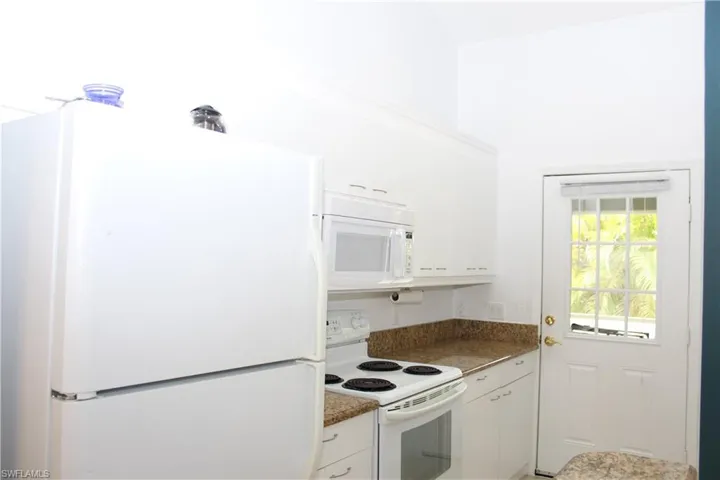 Kitchen with white cabinets, white appliances, and dark stone counters