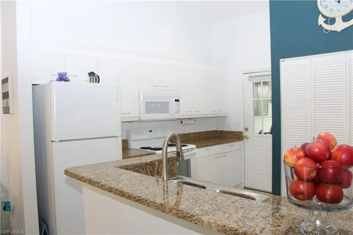 Kitchen featuring stone counters, white cabinetry, and white appliances