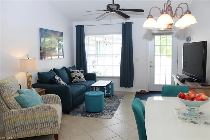 Living room featuring light tile patterned floors, ceiling fan with notable chandelier, and lofted ceiling