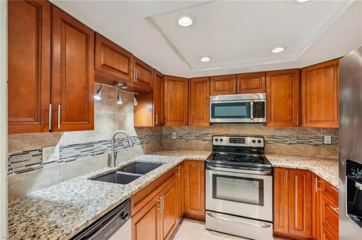 Kitchen with appliances with stainless steel finishes, light stone countertops, recessed lighting, and brown cabinets